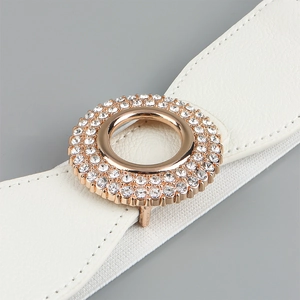 Detail of white elastic waist belt featuring a gold circular buckle with sparkling rhinestones