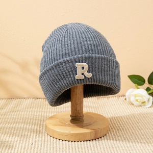 Berretto in maglia grigia con toppa R ricamata su un supporto per cappelli