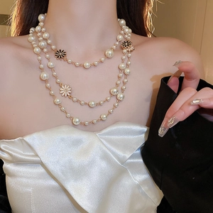 Close-up of triple-layered pearl necklace with white and black enamel daisy charms