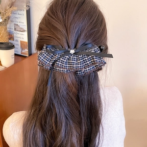 Detailed view of navy plaid hair clip with black bow on long hair in indoor setting