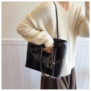 Detail of black leather tote bag with white contrast stitching and a small bear charm