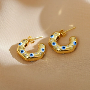 Detail shot of golden C-shaped hoop earrings with blue evil eye motifs and sparkling stones