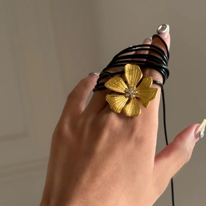 Detail of 18k gold flower pendant with brushed texture and rhinestones on black cord