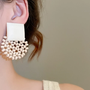 Close-up of cream white geometric beaded earrings featuring square and round accents