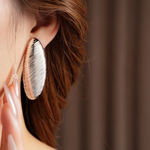 Close-up of a gold oval textured earring worn on the ear to show metallic detail