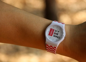 Close-up of a white fashion watch with a red and white checkered strap on a wrist