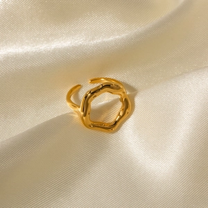 Detailed view of an 18K gold plated lava-style hollow flower ring on silk fabric