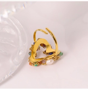 Detail of a gold adjustable heart ring featuring colorful gemstones and a fresh pearl