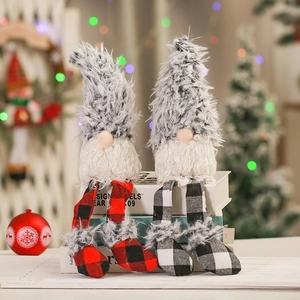 Pair of plush Christmas gnomes with long legs sitting on books by a warm holiday tree