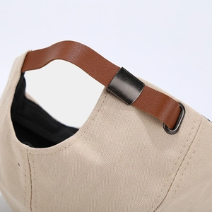 Dettaglio del berretto ottagonale in cotone beige con cinturino in pelle marrone