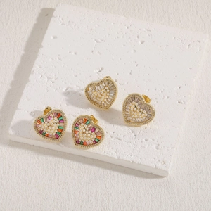 Boucles d'oreilles cœur dorées avec perles et gemmes colorées sur pierre de travertin
