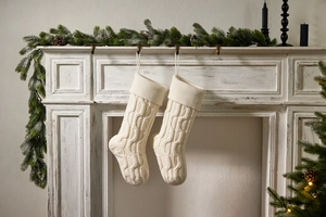 Detail of two cream knitted Christmas stockings with cable stitch on a mantelpiece