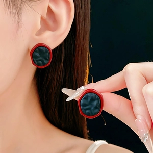 Détail de boucles d'oreilles irrégulières rouge et noir portées avec texture riche