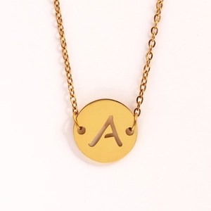 Détail macro du collier pièce dorée avec pendentif ajouré lettre A sur fond blanc pur