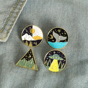 Creative enamel pin set featuring whale tail, UFO, mountains, and celestial nature designs