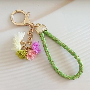 Detail of woven rope keychain featuring colorful fabric flower tassels and gold metal clasp