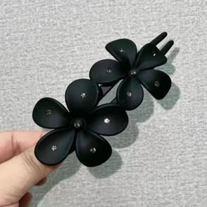 Close-up of elegant matte black acrylic hair clip with double flower and rhinestones