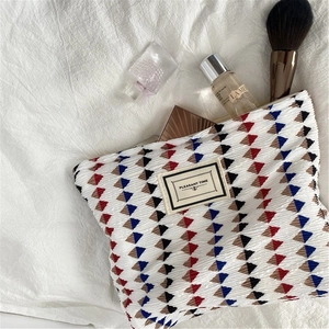 Detail view of white pleated chiffon makeup bag with colorful geometric patterns and fabric tag