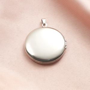 Polished silver stainless steel round locket pendant on pink silk background texture