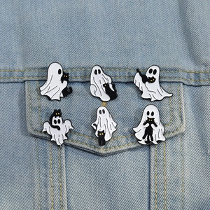 Detail of cartoon ghost and black cat enamel pins styled on a denim jacket pocket