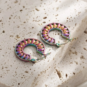 Detailed macro view of iridescent rainbow stainless steel leaf pattern earrings on a stone