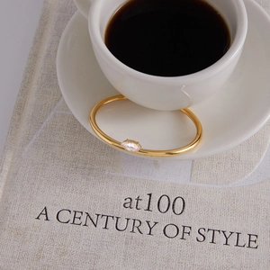 Detail of a gold-plated stainless steel bangle with an oval zircon resting on a white cup