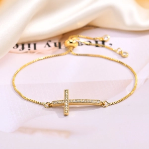 Detailed close-up of golden box chain bracelet with sparkling zircon cross on silk