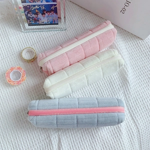 Macro detail of quilted plush pencil cases in pink, beige, and grey with soft texture