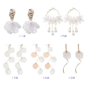 Boucles d'oreilles fleurs en nacre blanche avec détails dorés et pompons sur fond blanc