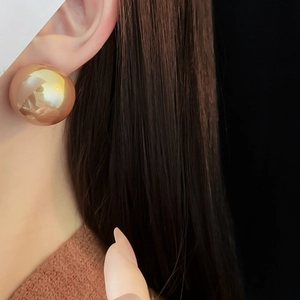 Close-up of a large polished gold sphere stud earring worn on the earlobe