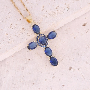 Dettaglio di un ciondolo a croce dorata con zirconi blu su una superficie di pietra
