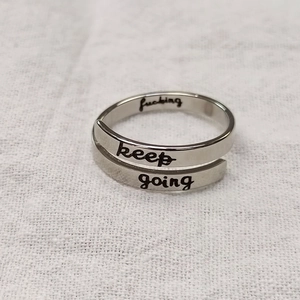 Macro detail of 'keep going' engraved silver adjustable stainless steel ring on fabric