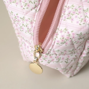 Close-up of golden zipper and pink floral quilted fabric on a portable makeup bag