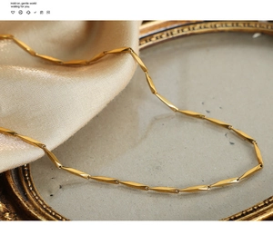Detailed close-up of golden bamboo link necklace on an elegant stone tray