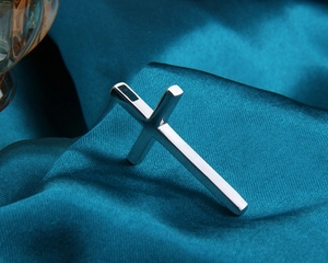 Macro shot of a silver cross pendant resting on turquoise satin fabric with high gloss finish