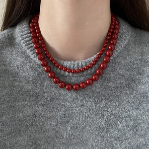 Gros plan d'un collier de perles rouges double rang sur un pull gris chic