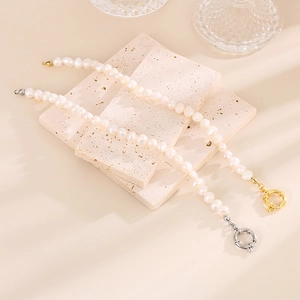 Détail de colliers en perles baroques sur pierre beige, montrant les fermoirs or et argent