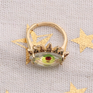 Detailed view of a gold Evil Eye ring with colorful zircons on a textured fabric