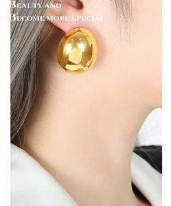Close-up of chunky gold dome earrings with a high-polished finish on female model
