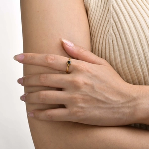 Close-up of a gold minimalist ring with a black round gemstone worn on a model's finger