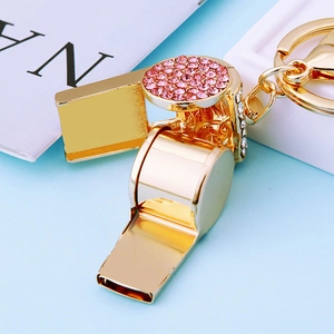 Golden metal whistle keychain with pink rhinestones and a polished finish on blue background