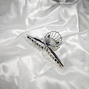 Detail of silver alloy hair claw clip with hollow shell design on white silk background