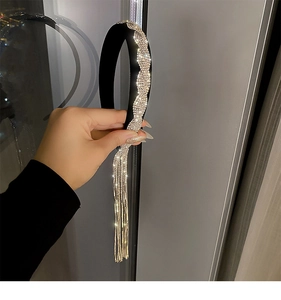 Détail d'un serre-tête large noir orné de strass ondulés et de longues chaînes à franges