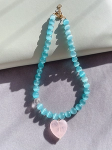 Macro shot of blue cat eye stone beads and large pink heart gemstone pendant necklace