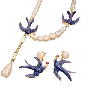 Vintage bird jewelry set with pearl necklace and blue enamel swallow earrings on white background