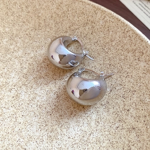 Macro shot of silver chunky C-shaped hoop earrings on textured ceramic dish