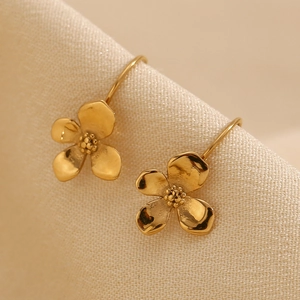 Detailed macro view of 18K gold plated flower dangle earrings on beige fabric