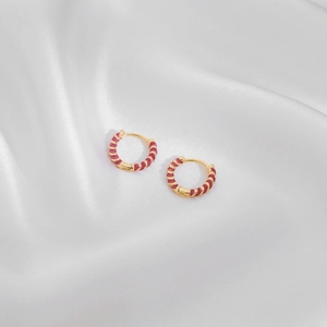 Detail of gold spiral hoop earrings with red enamel coating on white satin fabric
