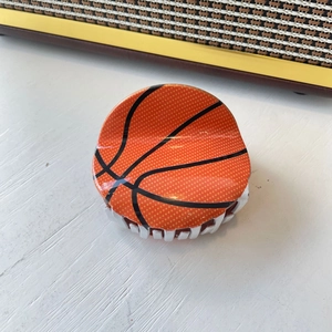 Detailed view of the orange basketball hair claw clip with black texture on white wood