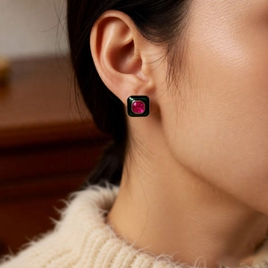 Close-up of green enamel square stud earring with a pink gemstone inlay on a model